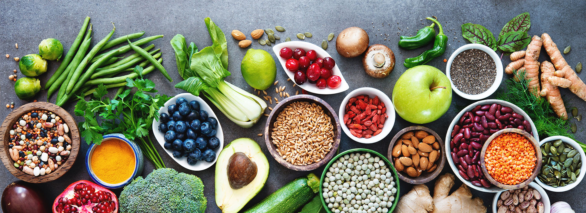 Vibrant array of fresh fruits and vegetables on a dark surface, with herbs and spices scattered around.