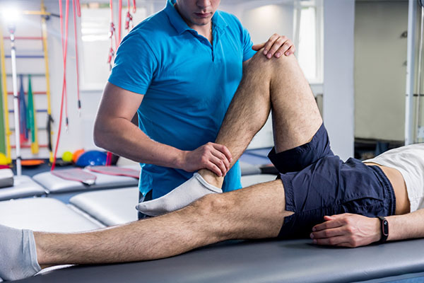 A man in a blue shirt is standing over a person lying on a massage table, working on their leg.