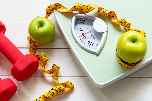 The image shows a table with various fitness items, including a scale, an apple, a dumbbell, and measuring tape, suggesting a focus on health and wellness.